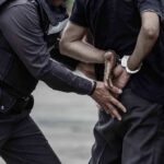 Police officer handcuffing a person against a vehicle