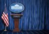 Network Alliance Exposed? DOJ Digs In White House press briefing podium with U.S. flag and blue curtain