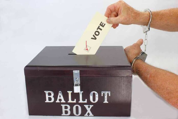 shutterstock_1187489227 Hand in handcuffs casting a vote into a ballot box
