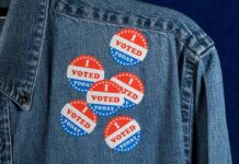 denim jacket with multiple red white and blue voting stickers