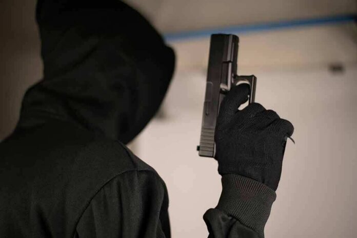 shutterstock_1495712093 Hooded person holding a handgun