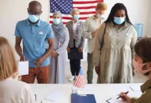 Phone Bill Voting? Minnesota Uproar Explodes Voters wearing masks stand in line at a polling station