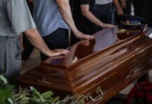 Mourners with hands on a polished wooden casket