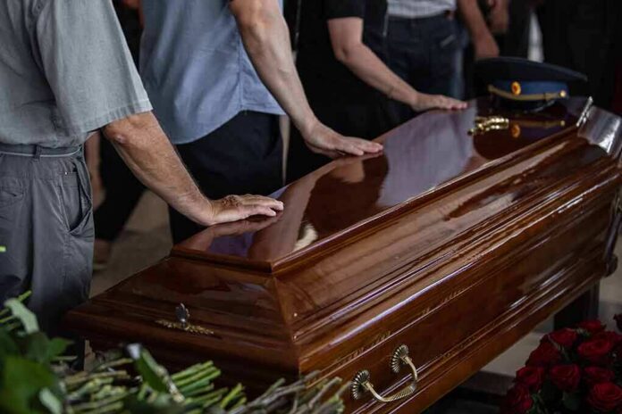 Mourners with hands on a polished wooden casket