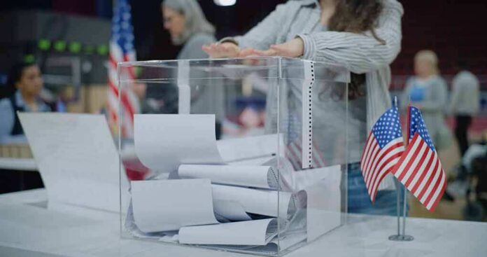 shutterstock_2454758129 Person casting a ballot into a clear box at a polling station