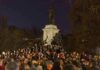 Crowd holding candles around a large statue at night