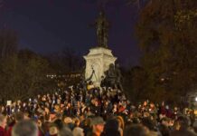 Crowd holding candles around a large statue at night