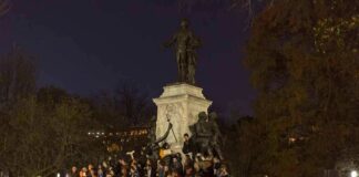 Crowd holding candles around a large statue at night