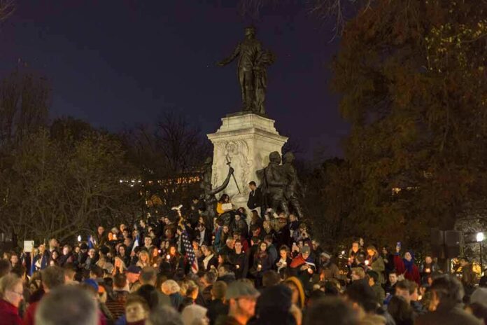 Crowd holding candles around a large statue at night