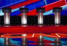 Maine Senate Rivals Clash Over War And Stocks Debate stage with four empty podiums and bright red and blue backdrop