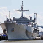 Large gray naval ship docked at an industrial port