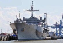 Large gray naval ship docked at an industrial port