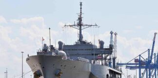 Large gray naval ship docked at an industrial port