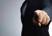 Person in a suit pointing directly at the camera