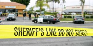yellow sheriff's line tape blocks a street near police cars